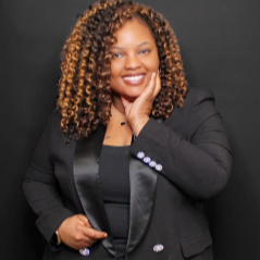 African American woman with curly hair smiling wearing a brown and black patterned shirt.